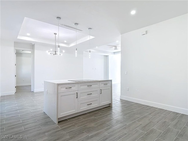 kitchen featuring a kitchen island, baseboards, hanging light fixtures, wood tiled floor, and a tray ceiling