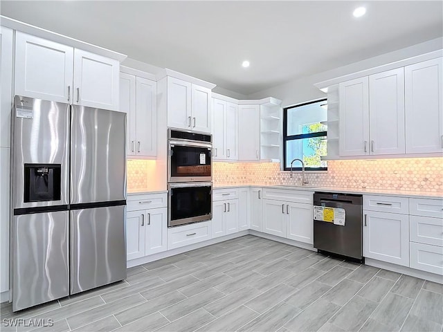 kitchen featuring appliances with stainless steel finishes, a sink, light countertops, open shelves, and backsplash