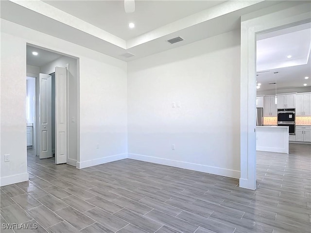 spare room featuring baseboards, visible vents, and a raised ceiling