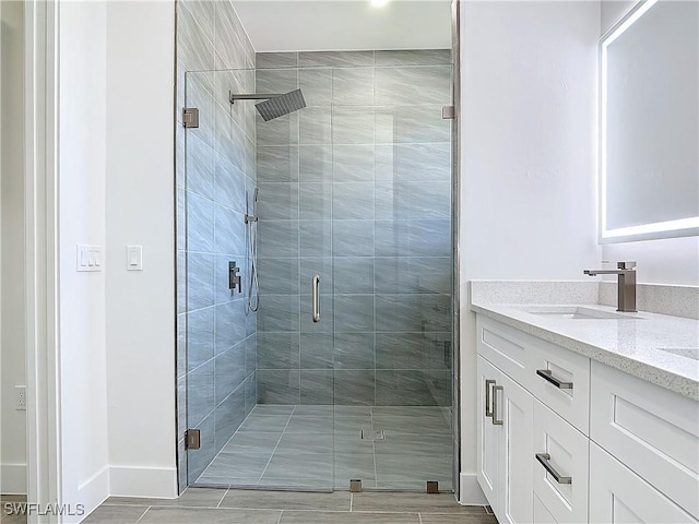 bathroom featuring a stall shower, a sink, baseboards, and double vanity