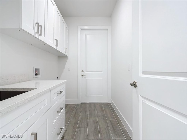 clothes washing area with hookup for a washing machine, wood tiled floor, baseboards, and cabinet space