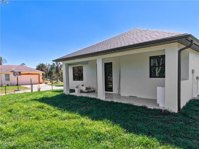 back of house featuring a shingled roof, a lawn, a patio, and stucco siding