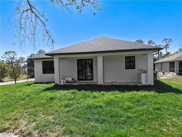 back of house with a shingled roof, a lawn, and stucco siding