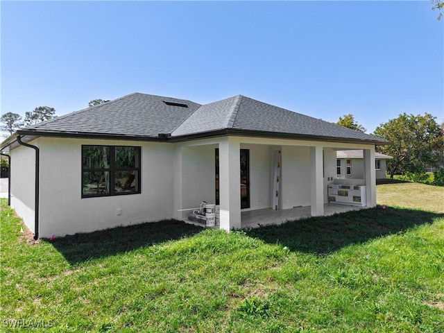 back of property with a patio, a shingled roof, a lawn, and stucco siding