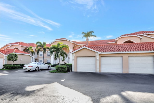 mediterranean / spanish house featuring community garages, a tile roof, and stucco siding