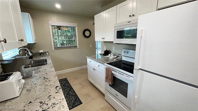 kitchen with light stone counters, white appliances, a sink, baseboards, and white cabinets