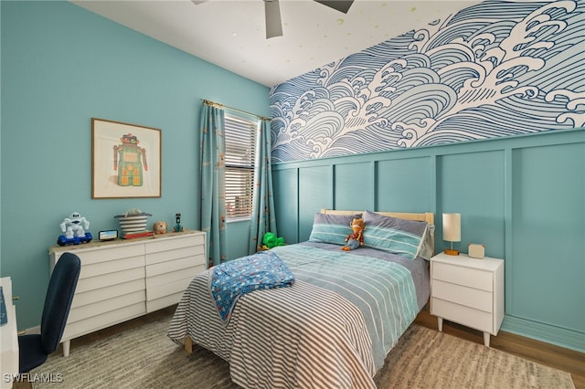 bedroom with ceiling fan, a wainscoted wall, a decorative wall, and wood finished floors