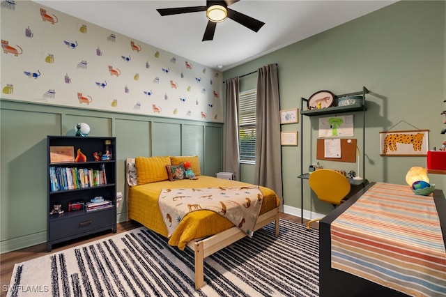 bedroom featuring a wainscoted wall, ceiling fan, wallpapered walls, and wood finished floors