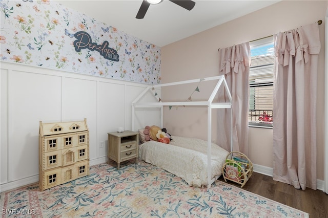 bedroom featuring a decorative wall, a wainscoted wall, wood finished floors, a ceiling fan, and wallpapered walls