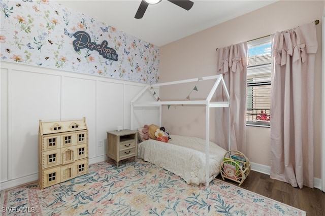 bedroom featuring a wainscoted wall, a decorative wall, wood finished floors, and wallpapered walls