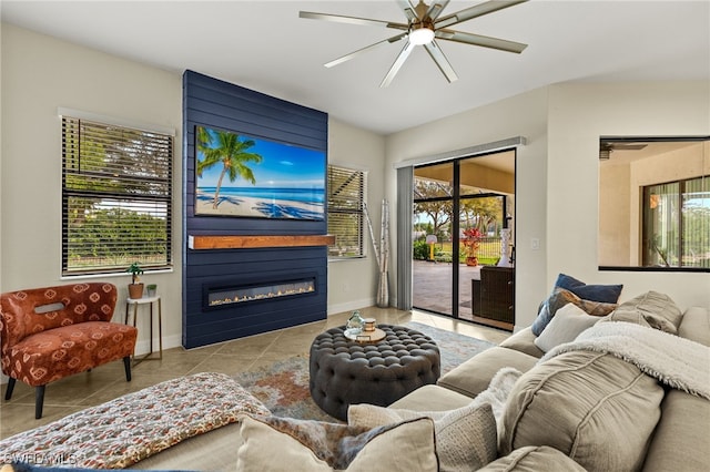 tiled living area featuring a large fireplace, ceiling fan, and baseboards