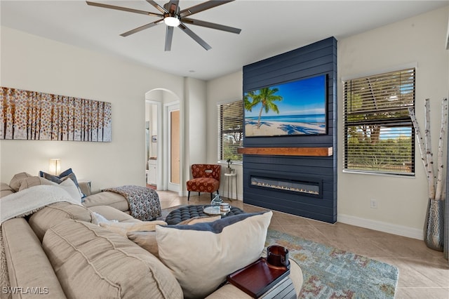 tiled living room featuring baseboards, arched walkways, ceiling fan, and a large fireplace