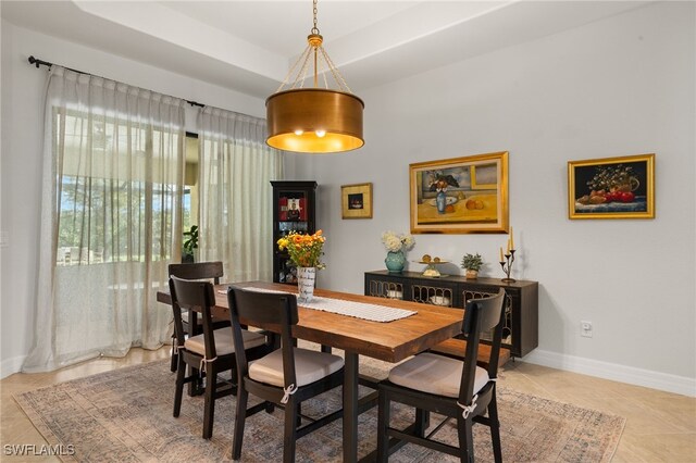 dining space with a tray ceiling, light tile patterned flooring, and baseboards