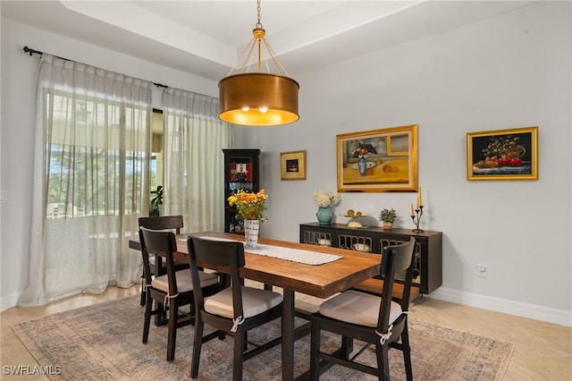 dining space with baseboards, a tray ceiling, and light tile patterned floors
