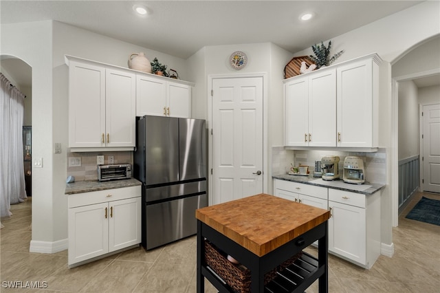 kitchen featuring arched walkways, tasteful backsplash, freestanding refrigerator, and white cabinetry