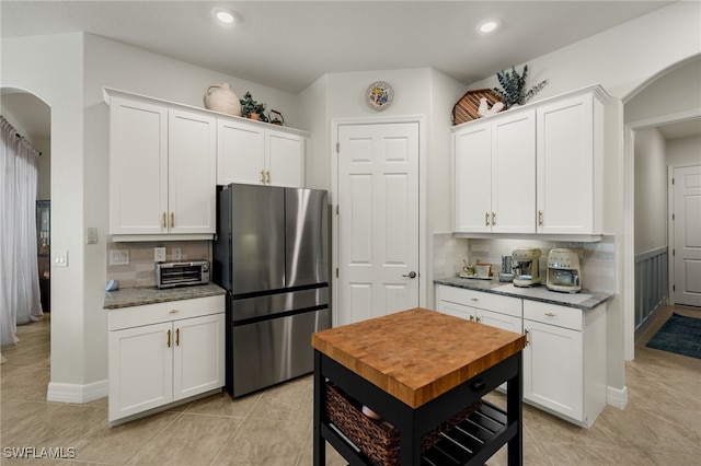 kitchen featuring freestanding refrigerator, white cabinets, arched walkways, and tasteful backsplash