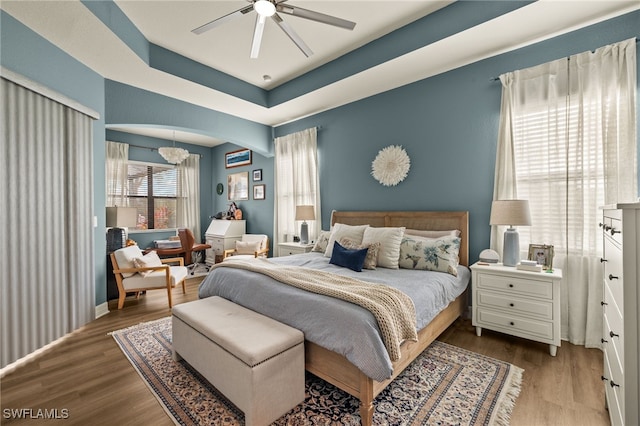 bedroom with a tray ceiling, arched walkways, wood finished floors, and ceiling fan