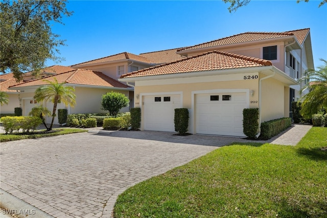 mediterranean / spanish house featuring a tiled roof, a front yard, stucco siding, decorative driveway, and a garage