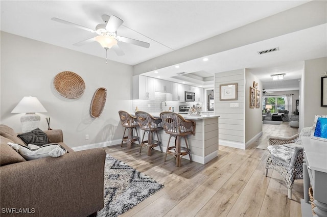 living area featuring light wood-style floors, baseboards, visible vents, and a ceiling fan