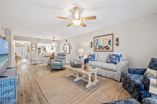 living room featuring light wood-type flooring, baseboards, and a ceiling fan