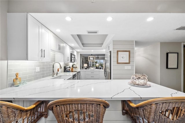 kitchen with light stone counters, stainless steel appliances, a raised ceiling, visible vents, and a peninsula