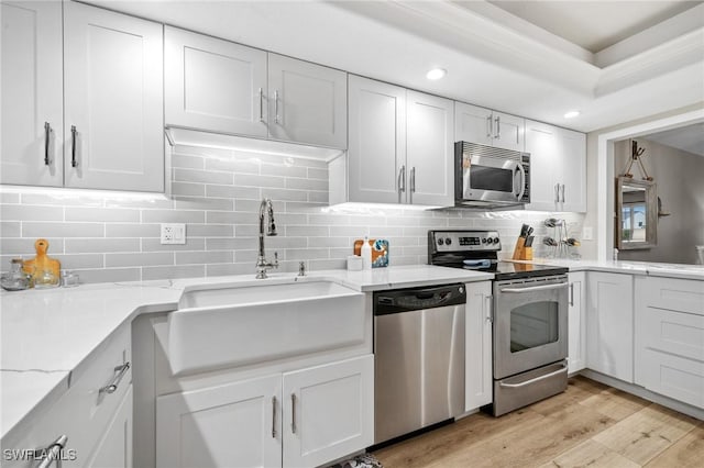 kitchen featuring tasteful backsplash, white cabinets, light wood-style flooring, appliances with stainless steel finishes, and a sink