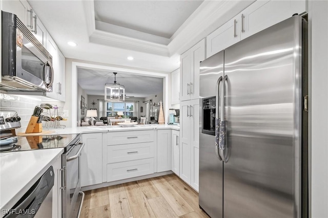 kitchen featuring light wood-type flooring, a tray ceiling, stainless steel appliances, and light countertops