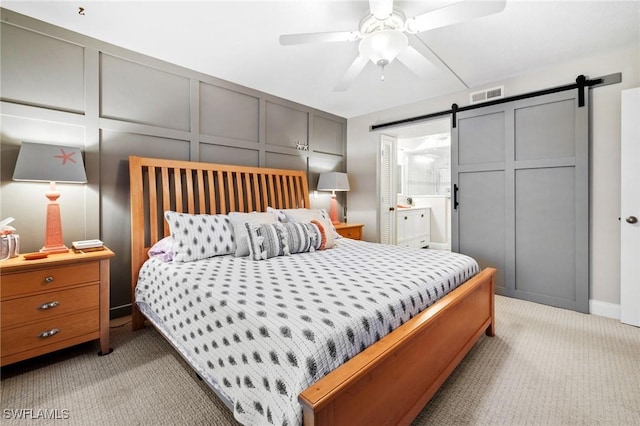 bedroom featuring ceiling fan, a barn door, a decorative wall, light carpet, and visible vents