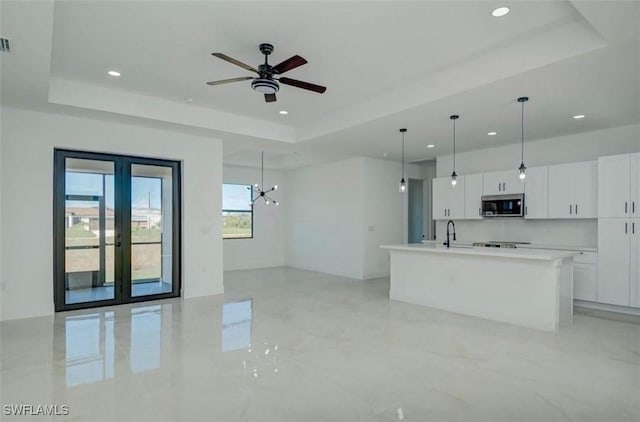 kitchen with stainless steel microwave, open floor plan, hanging light fixtures, white cabinetry, and a raised ceiling