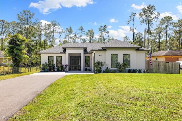 prairie-style home with driveway, fence, a front lawn, and stucco siding