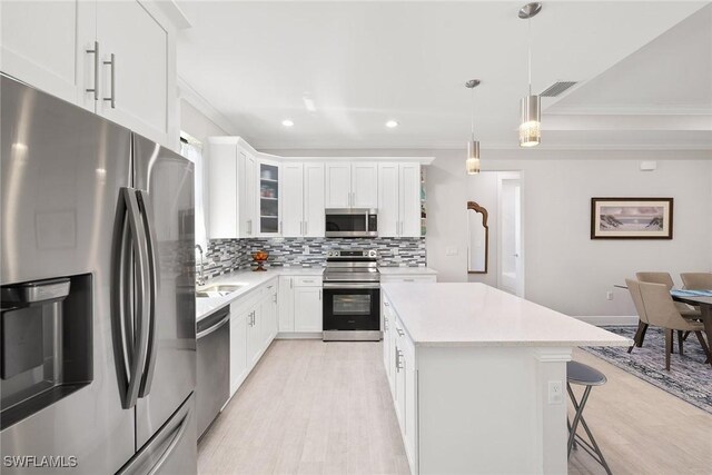 kitchen with stainless steel appliances, light countertops, a center island, tasteful backsplash, and crown molding