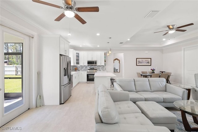 living area featuring visible vents, light wood-style flooring, ornamental molding, a tray ceiling, and recessed lighting