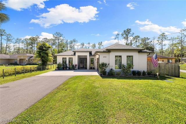 rear view of property featuring a yard, aphalt driveway, fence, and stucco siding