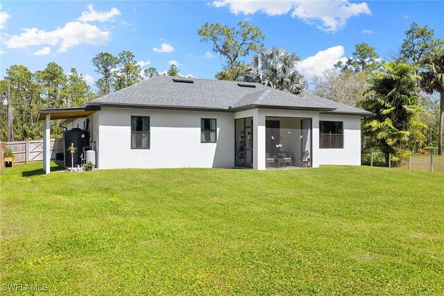 rear view of property featuring a sunroom, stucco siding, a yard, and fence