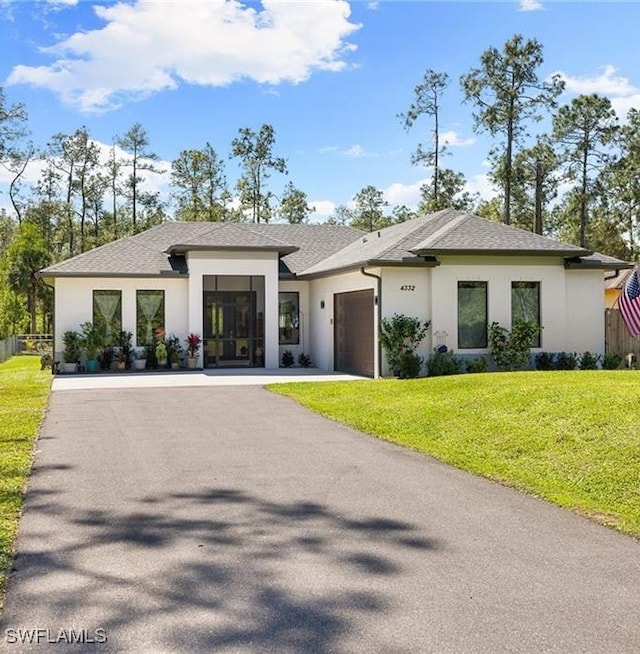 view of front facade featuring aphalt driveway, stucco siding, a shingled roof, an attached garage, and a front lawn