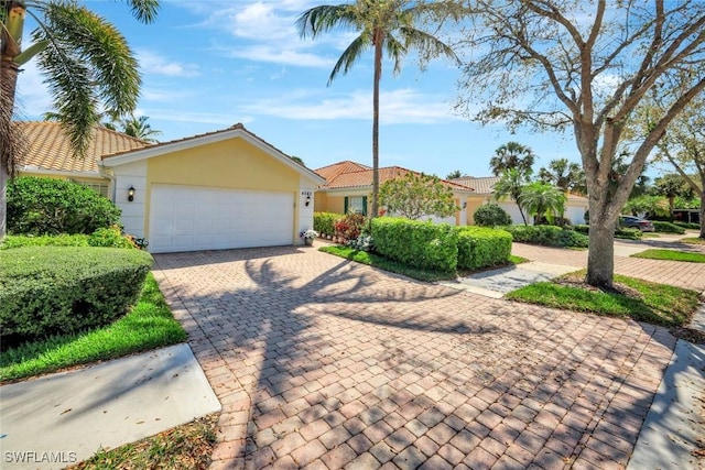 view of front of house featuring decorative driveway, an attached garage, a tile roof, and stucco siding