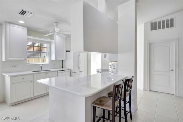 kitchen with white appliances, a sink, visible vents, and a kitchen breakfast bar