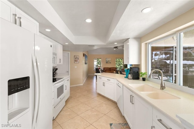 kitchen featuring white appliances, white cabinets, a tray ceiling, a sink, and recessed lighting