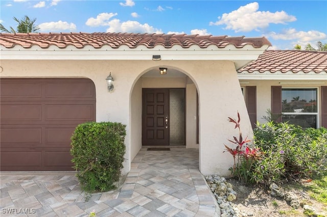 view of exterior entry with a garage, a tile roof, and stucco siding