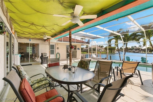 view of patio / terrace with a lanai, area for grilling, a water view, a ceiling fan, and an outdoor pool