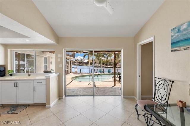 doorway to outside with light tile patterned floors, lofted ceiling, ceiling fan, a sink, and baseboards