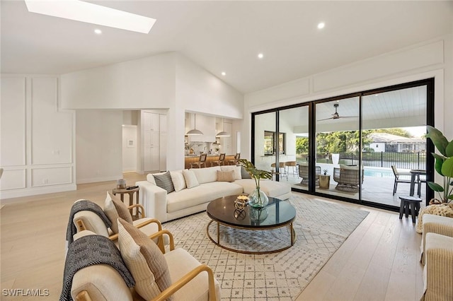 living area featuring a skylight, recessed lighting, a decorative wall, high vaulted ceiling, and light wood-type flooring