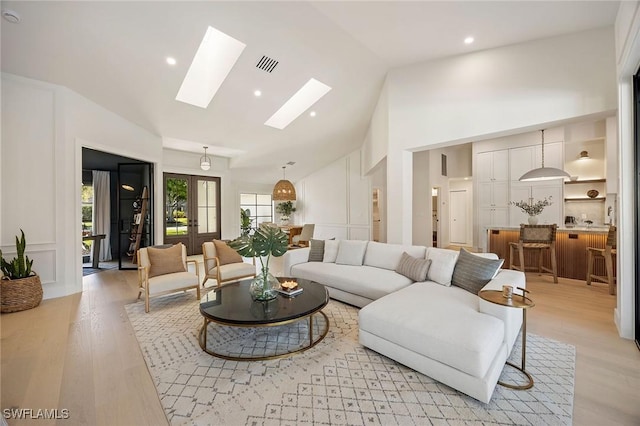 living room with a skylight, light wood finished floors, visible vents, french doors, and high vaulted ceiling