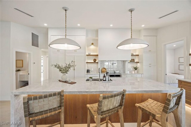 kitchen with visible vents, decorative backsplash, white cabinetry, open shelves, and a sink