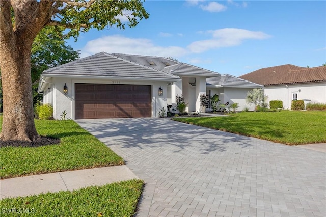 single story home with a garage, a tile roof, decorative driveway, stucco siding, and a front yard