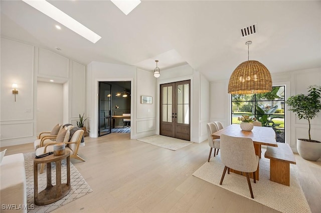 dining area with light wood-style flooring, visible vents, a decorative wall, and french doors