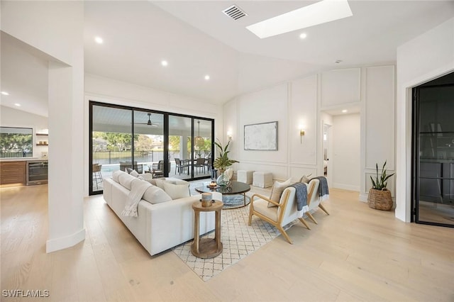 living room featuring lofted ceiling with skylight, wine cooler, visible vents, and plenty of natural light