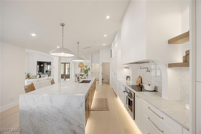 kitchen with a spacious island, light wood-style floors, white cabinetry, oven, and black electric cooktop