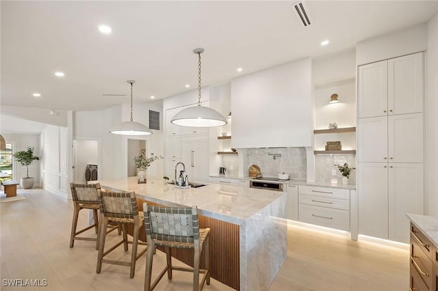 kitchen with a sink, visible vents, decorative backsplash, open shelves, and light wood finished floors