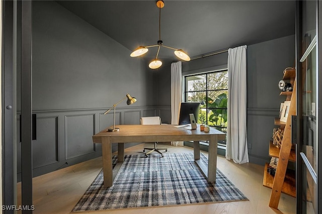 home office with a wainscoted wall, vaulted ceiling, a decorative wall, and wood finished floors